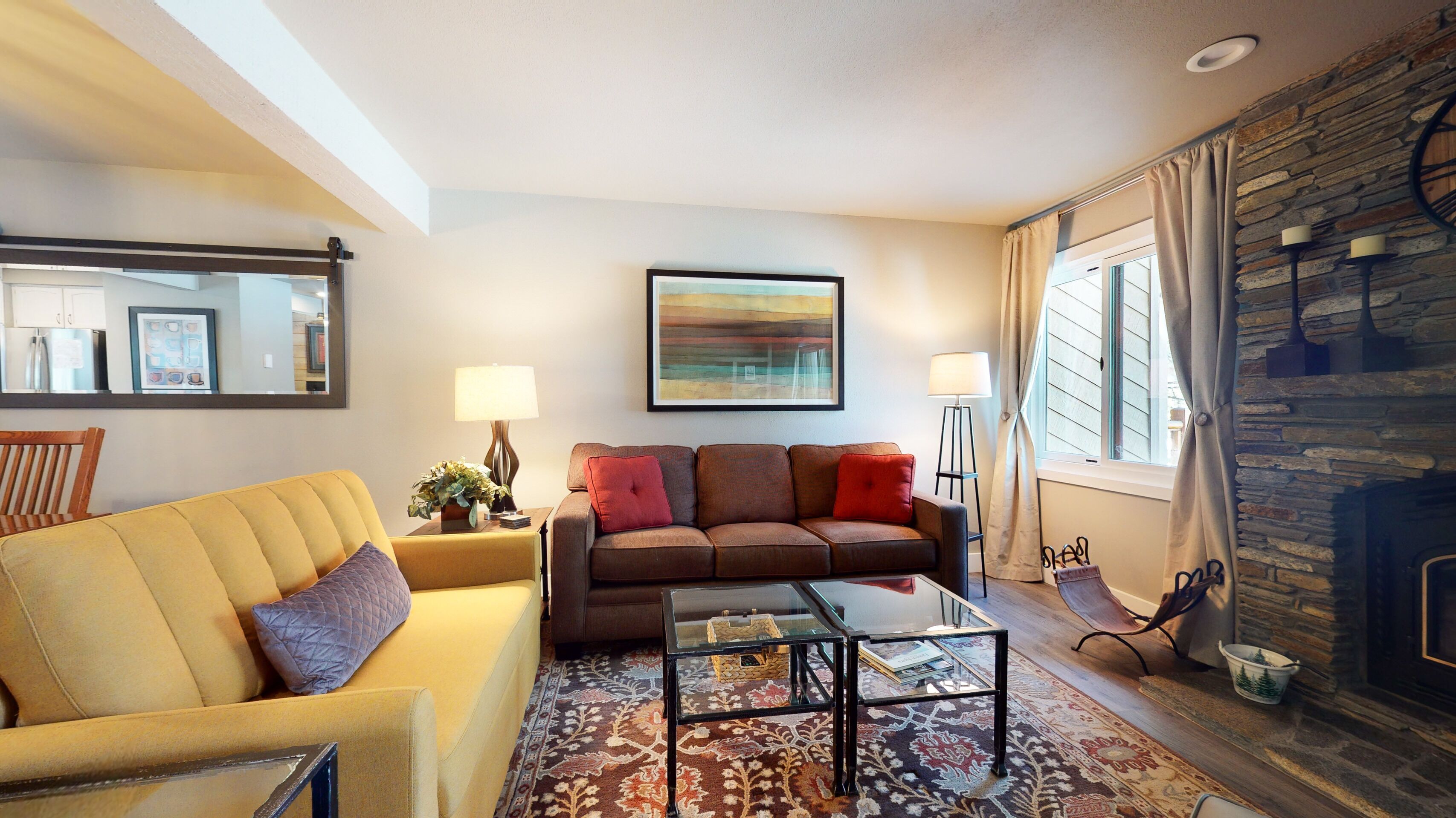 A living room with a sofa, a glass coffee table, a fireplace, and a large abstract painting on the wall.
