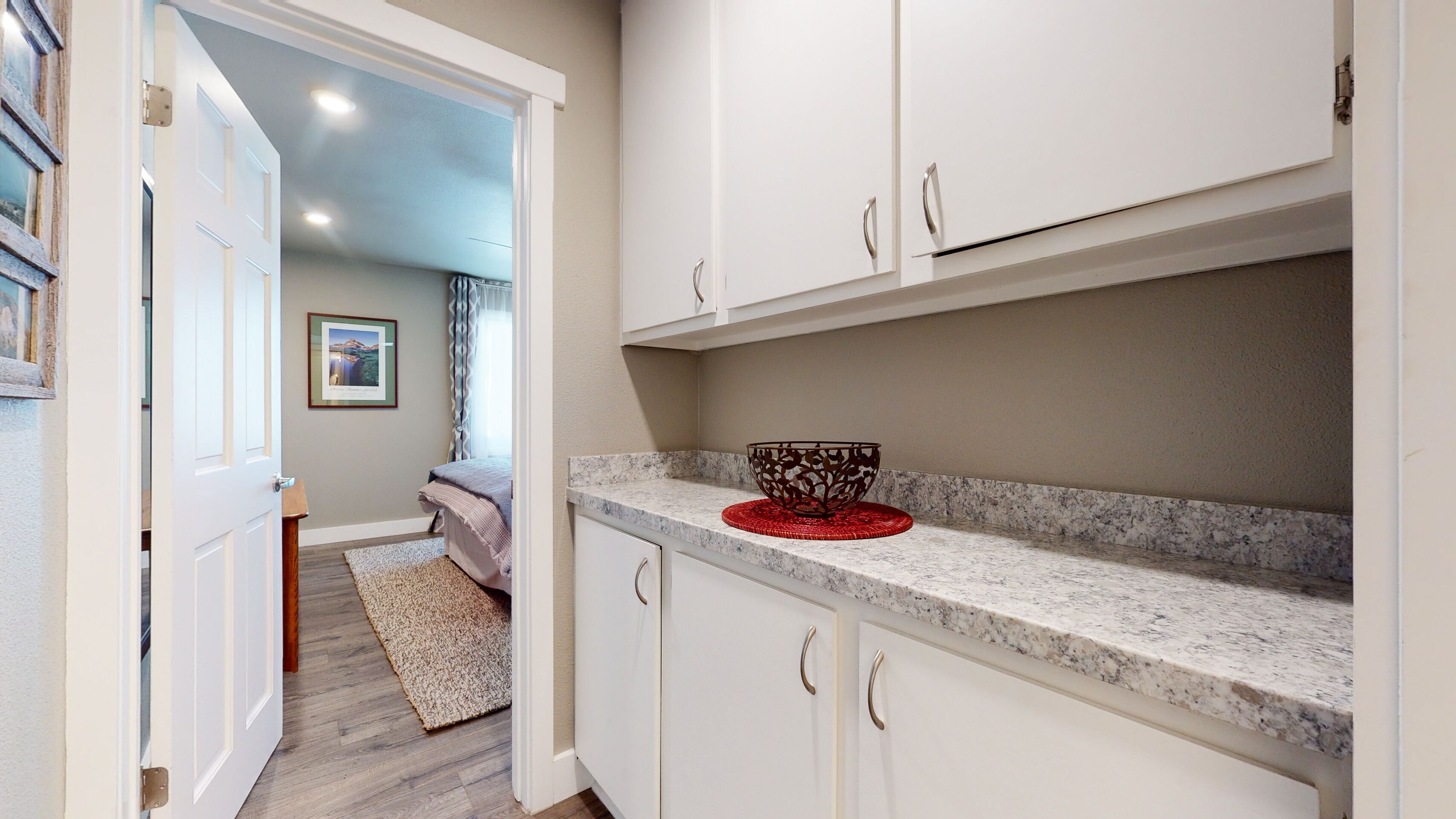 Una cocina con armarios blancos, encimera de granito y un cuenco decorativo rojo.