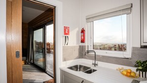A modern kitchen with a large window, a sink, and a fire extinguisher. - Hilltop Lodge (Corwen)