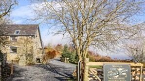 A rustic stone building with a gravel driveway leading to a wooden gate. A signboard reads "Welcome to the Hidden Meadow at Hapotty Glynnen Luxury Rural Retreat." - Hilltop Lodge (Corwen)