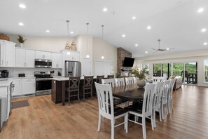 Una cocina moderna con gabinetes blancos, electrodomésticos de acero inoxidable y una zona de comedor con sillas blancas y una mesa negra.