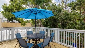 A deck with a round table and chairs, a blue umbrella, and a white railing. - Cloud Suite on Duval Street with Balcony (Key West)