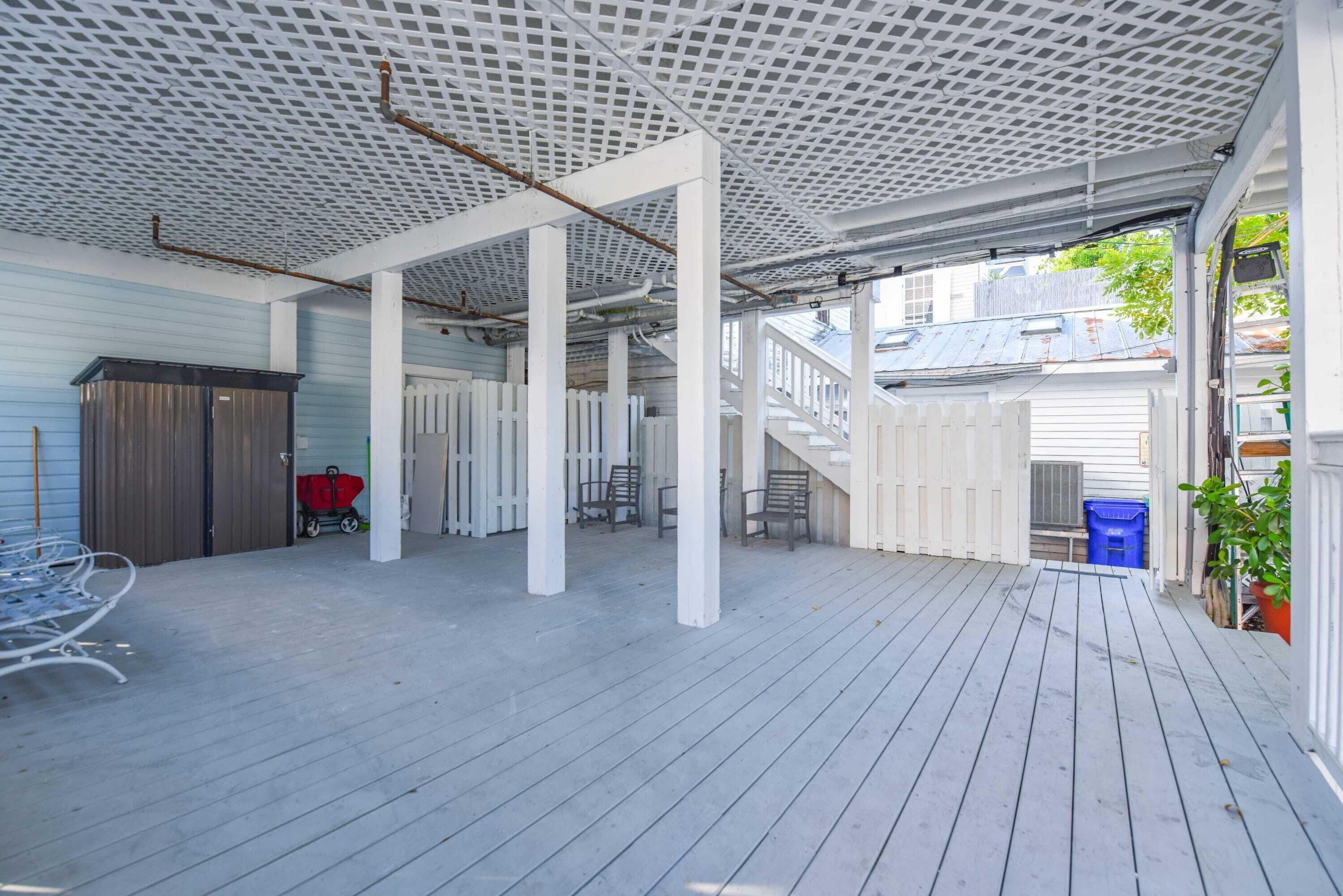 Un patio techado al aire libre con cubierta de madera, barandillas blancas y cerca blanca.