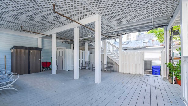 An outdoor covered patio with a wooden deck, white railings, and a white fence. - Cloud Suite on Duval Street with Balcony (Key West)