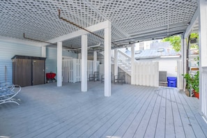 An outdoor covered patio with a wooden deck, white railings, and a white fence.