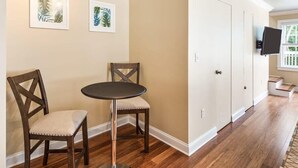 A room with a wooden floor, a round table with two chairs, a door, and a TV mounted on the wall. - Cloud Suite on Duval Street with Balcony (Key West)