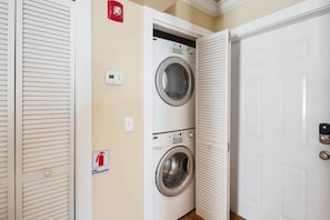 A laundry room with two stacked washing machines, a fire extinguisher sign, and a door with a keypad lock.