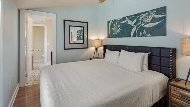 A bedroom with a bed, a ceiling fan, a wall-mounted lamp, and a framed picture. - Cloud Suite on Duval Street with Balcony (Key West)