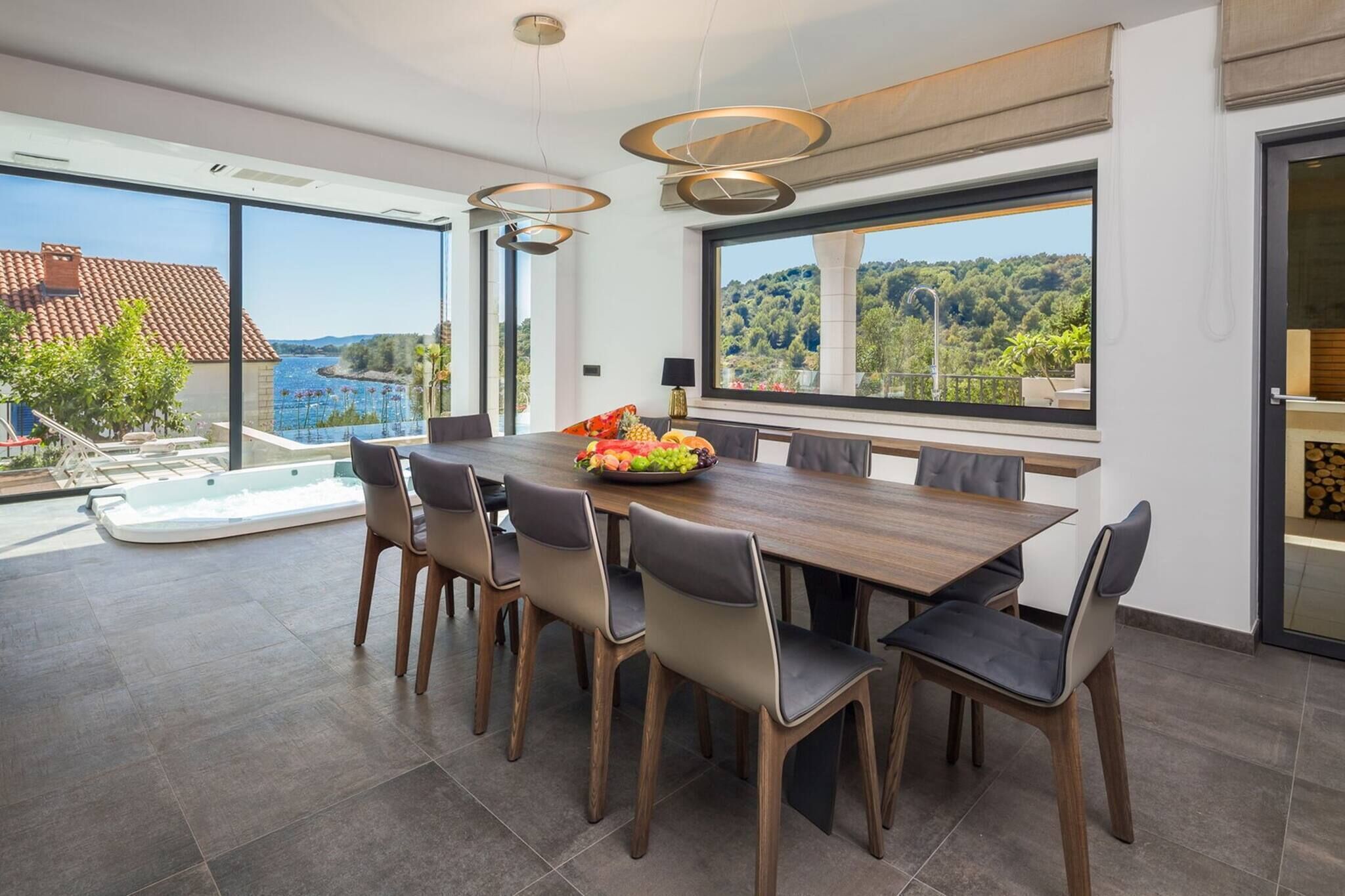 A modern dining area with a large table, chairs, and a view of a pool and mountains.