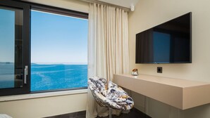 A hotel room with a large window offering a sea view, a modern chair, a flat-screen TV, and a minimalist counter. - Luxury Seafront Villa Blue Heaven Ciovo with Pool (Okrug Gornji)