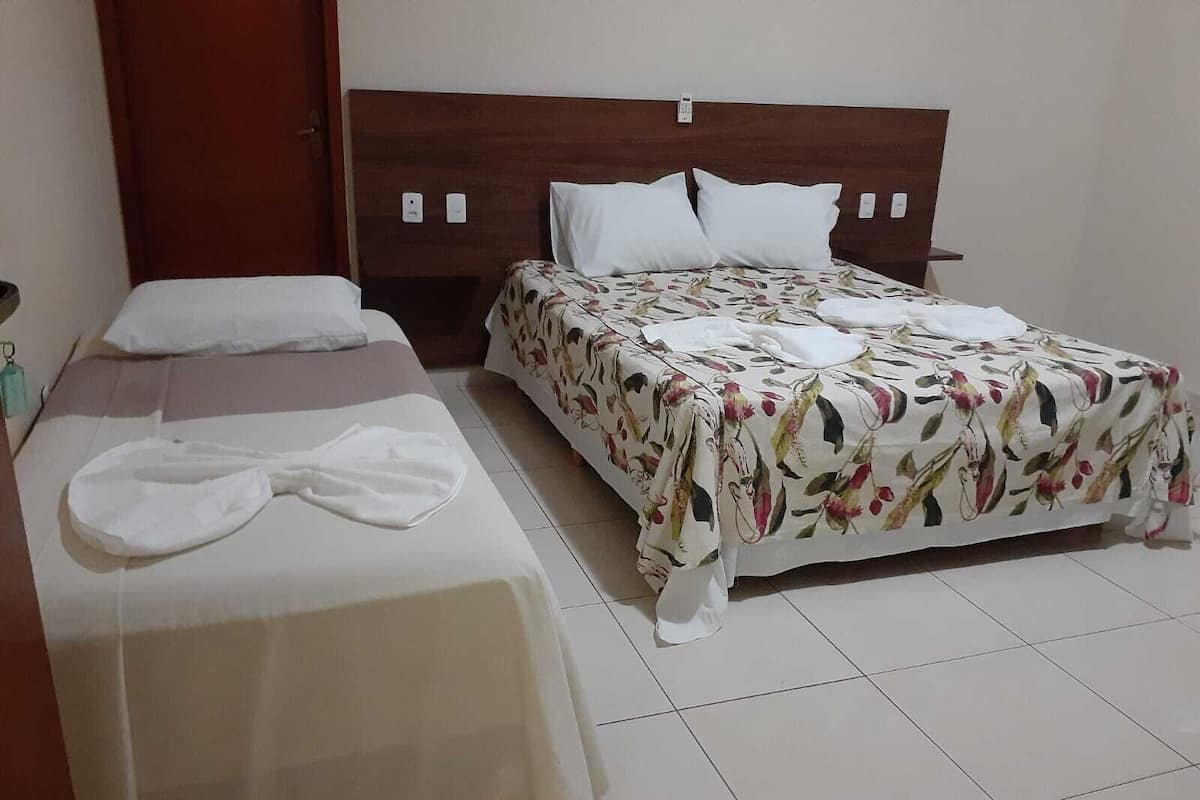 A hotel room with two beds, one with a floral bedspread and the other with a plain white bedspread.