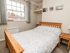 A bedroom with a wooden bed, a radiator, a window with curtains, and three wall-mounted pictures. - Keepers Cottage, 21 Coppergate (Driffield)