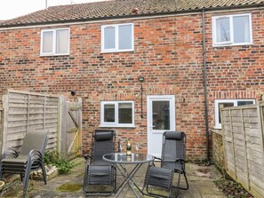 A brick house with two windows, a door, and a small patio with two chairs and a table. - Keepers Cottage, 21 Coppergate (Driffield)