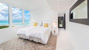 A modern bedroom with a large bed, white bedding, and two yellow pillows. It features a large window with a view of the ocean and a ceiling with recessed lighting. - Oceanview Private Condo at The Setai -190102 (Miami Beach)