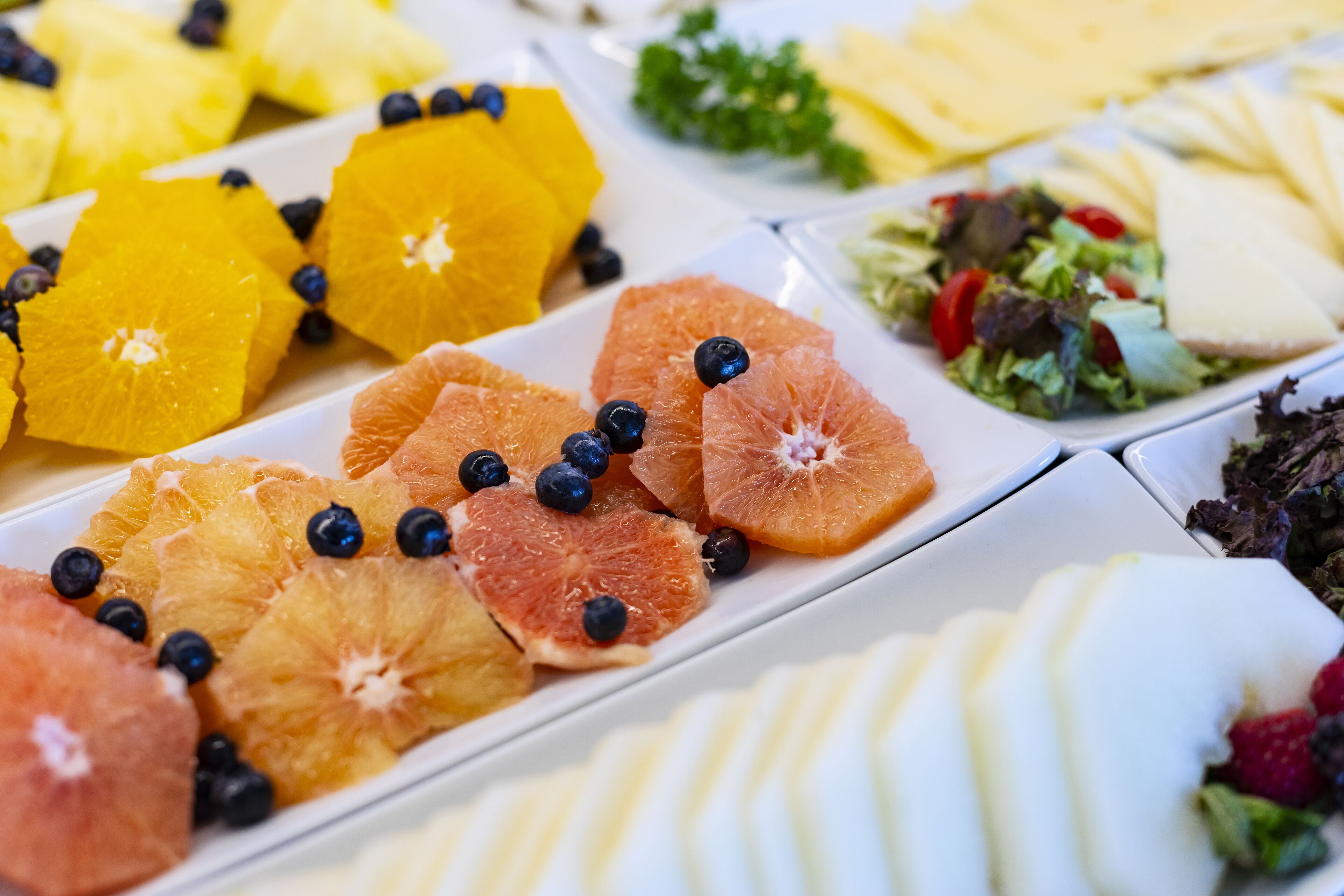Diverse soorten fruit en groenten, gerangschikt op borden, waaronder sinaasappels, blauwe bessen en bladgroenten.