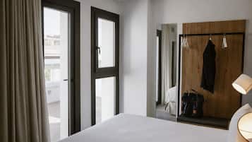 Hotelkamer met een bed, een houten garderobe, een spiegel, een kapstok en een raam met gordijnen.