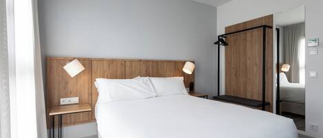 Una habitación de hotel moderna con una cama grande, mesitas de noche, un espejo y un cabecero de madera.