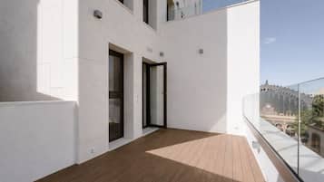 Un balcón moderno con suelo de madera, barandilla de vidrio y vista a un edificio histórico.