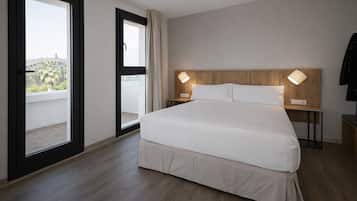Habitación de hotel con una cama grande, cabecera de madera, dos lámparas de noche, mesitas de noche, puerta corrediza de vidrio a un balcón y vistas a palmeras.