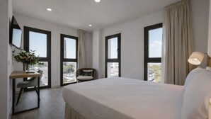 A hotel room with a large bed, a desk with a vase of flowers, a chair, and large windows with curtains. - Petit Palace Vargas (Seville)