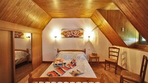 A cozy attic bedroom with a wooden sloped ceiling, a bed with a striped blanket, two wall-mounted lights, and a floral painting on the wall.