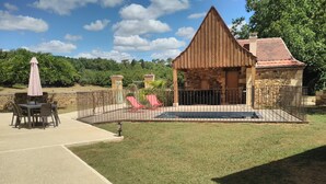 A backyard with a stone patio, a pool, and a wooden structure.