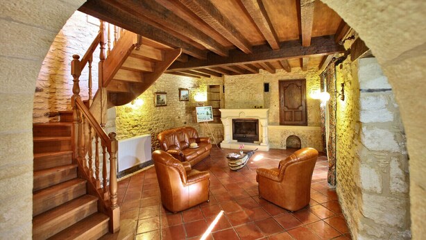 A rustic interior with a stone fireplace, leather sofas, and a wooden staircase.