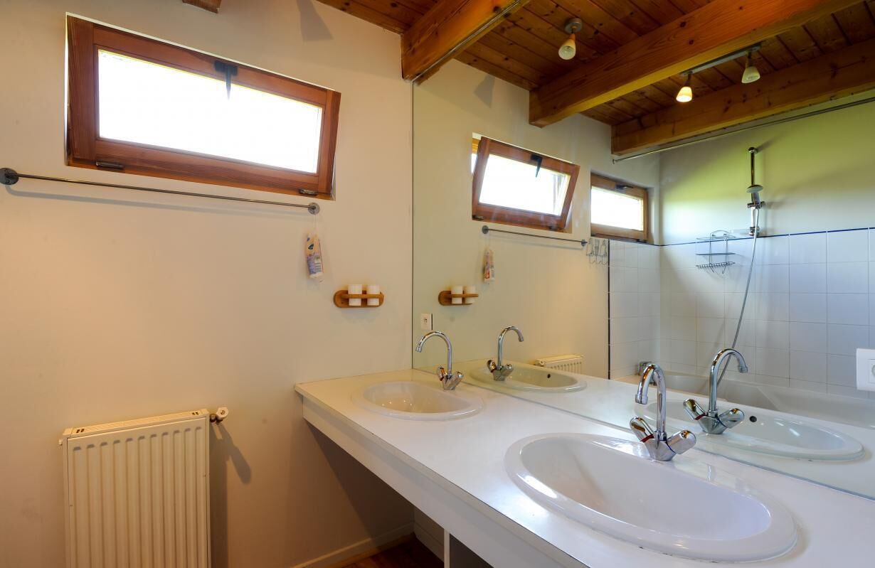 Une salle de bain avec deux lavabos, un miroir, une douche et des poutres en bois au plafond.