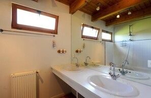 Baño con dos lavamanos, un espejo, ducha y vigas de techo de madera.