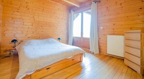 Un dormitorio de cabaña de madera con cama, mesita de noche, cómoda y ventana con cortinas.