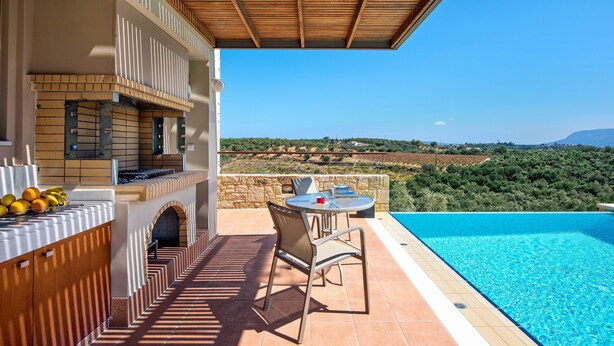 Un espace aménagé au bord de la piscine, avec un barbecue, des sièges d’extérieur et une vue sur la campagne.