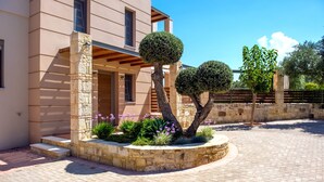 Un bâtiment moderne avec une façade en pierre, une cour pavée et des arbres taillés en formes géométriques.