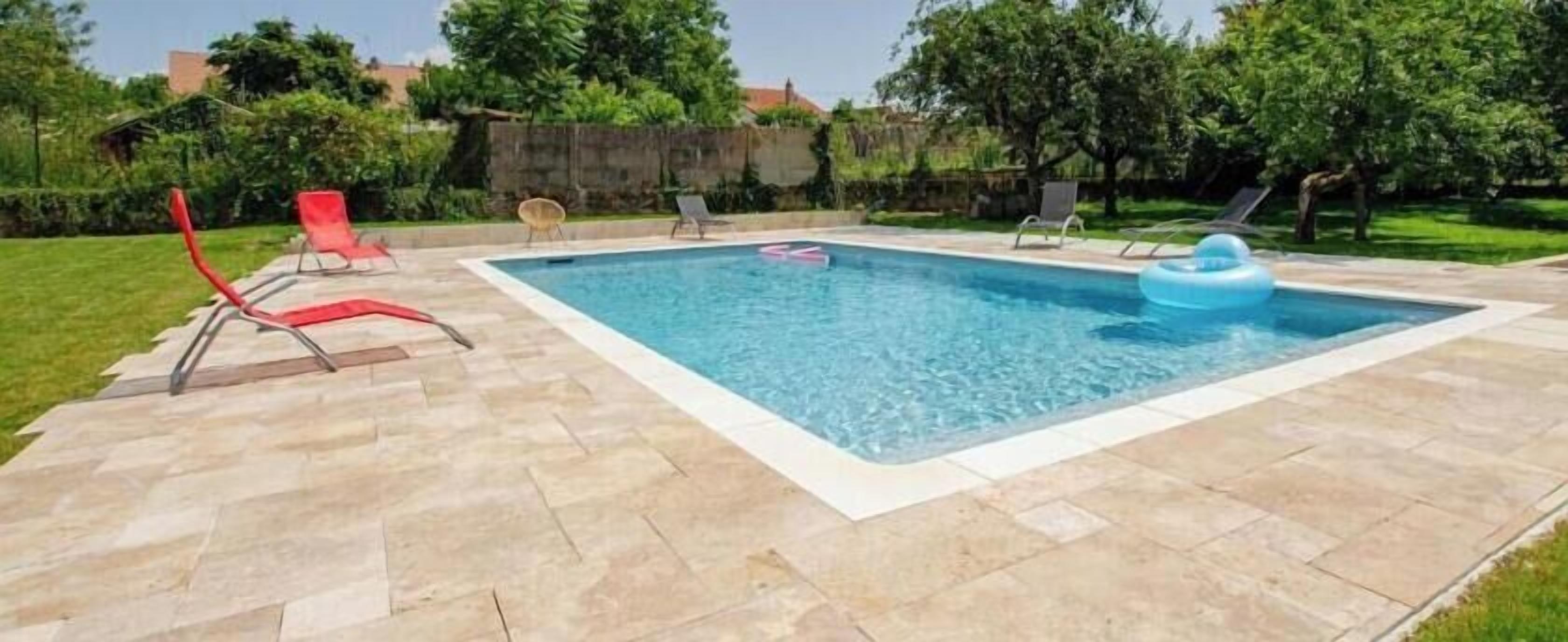 Une piscine rectangulaire avec une terrasse carrelée, entourée de chaises longues et d’une pelouse.