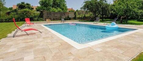 Une piscine rectangulaire avec une terrasse carrelée, entourée de chaises longues et d’une pelouse.