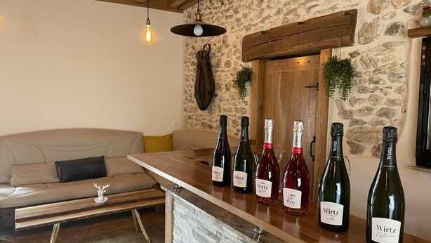 A cozy living room with a stone wall, a wooden bench, a sofa, and a wine bar with several bottles of wine. - Le Gite du Pigeonnier (VILLENAUXE LA GRANDE)