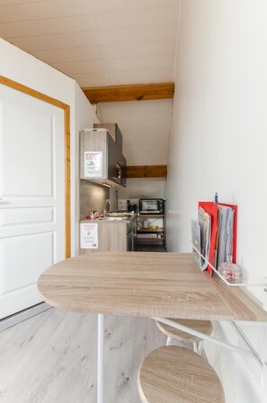 A compact kitchen with a wooden table, a microwave, and a red bulletin board.