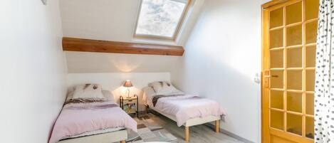 A small, cozy room with two single beds, a table, a lamp, and a window with a view of the sky.