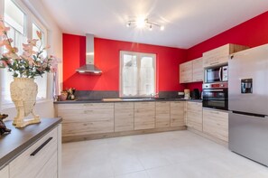 Una cocina moderna con armarios de madera clara, un refrigerador de acero inoxidable y una pared de acento roja.