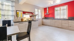 Una cocina moderna con una pared roja de acento, un comedor con una silla negra y una ventana con cortinas a rayas.