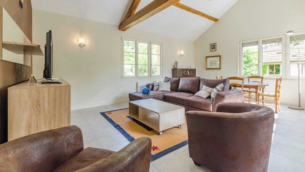 A spacious living room with a high ceiling, wooden beams, a large sofa set, a coffee table, and a dining area with chairs and a table.