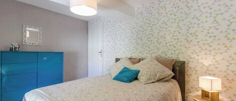 Une chambre à coucher avec un lit, une table de chevet, une commode et un miroir au mur.