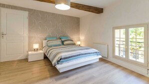 A bedroom with a bed, bedside tables, a window with a view, and a wooden ceiling beam.