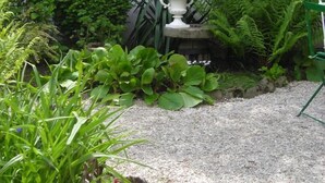 Un jardín con diversas plantas, un jarro blanco y un camino de grava.