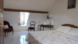 Un dormitorio con una cama, dos sillas, una mesa y una ventana.