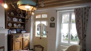 Un comedor con un aparador de madera, una mesa con mantel decorativo, una silla y una ventana con cortinas.