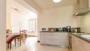 Una cuina moderna amb una illa central, electrodomèstics integrats i zona de menjador amb taula i cadires.