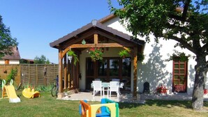 A covered patio with a table and chairs, a play structure, and a wooden fence. - Le Nid - Rouilly Sacey (ROUILLY SACEY)