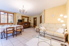 A living room with a sofa, dining table, chairs, a chandelier, and a television.