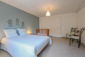 A bedroom with a bed, a crib, a chair, and a door. - Le Gite de la CEA - SAINT MARDS EN OTHE (SAINT MARDS EN OTHE)