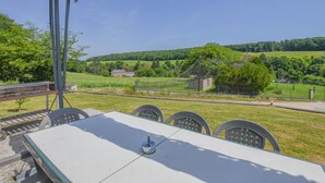 Ein Tisch mit Stühlen im Freien, mit Blick auf eine ländliche Landschaft aus Feldern und einem kleinen Gebäude.